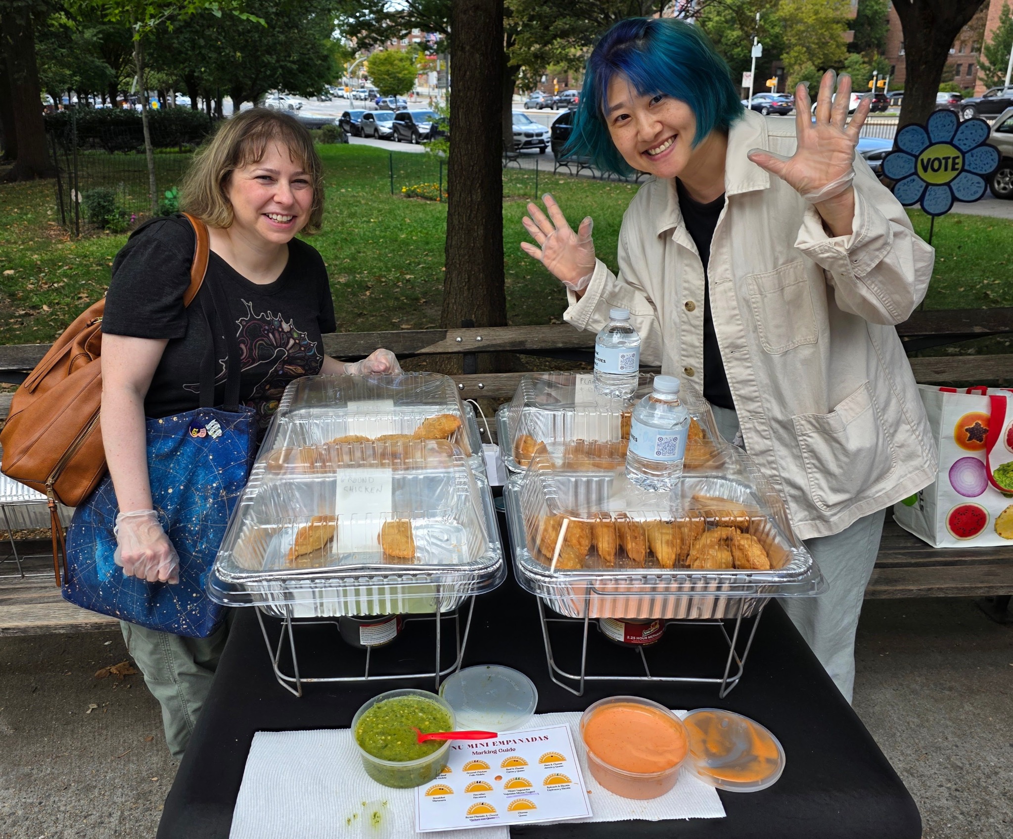 Two volunteers welcome neighbors at the empanada table at VOTEFEST 2.0.